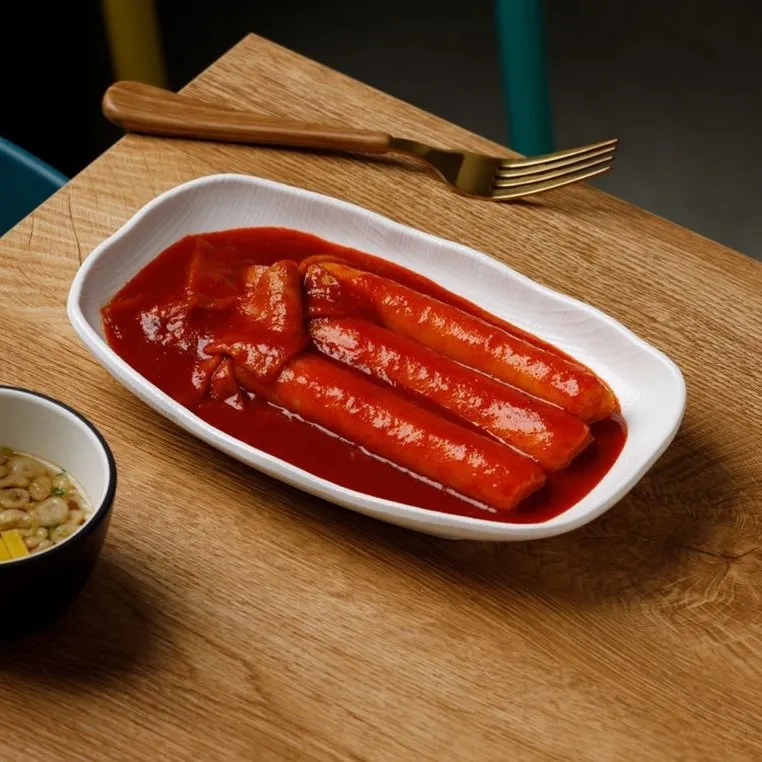 지우분식 떡볶이. 흰 접시에 굵은 가래떡과 넓적한 어묵이 붉은 국물에 잠겨 있다.