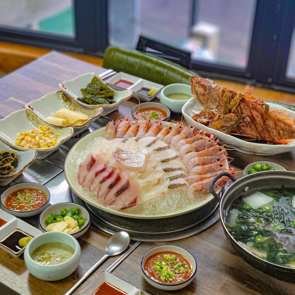 바다뷰가문동포구횟집애월 창가 자리에 차려진 상. 회 한 접시와 튀김, 국그릇 둘, 종지 여럿, 밑반찬이 함께 놓여 있다. 제주 제주시 애월읍 가문동길 43, 전화 010-2168-6527.