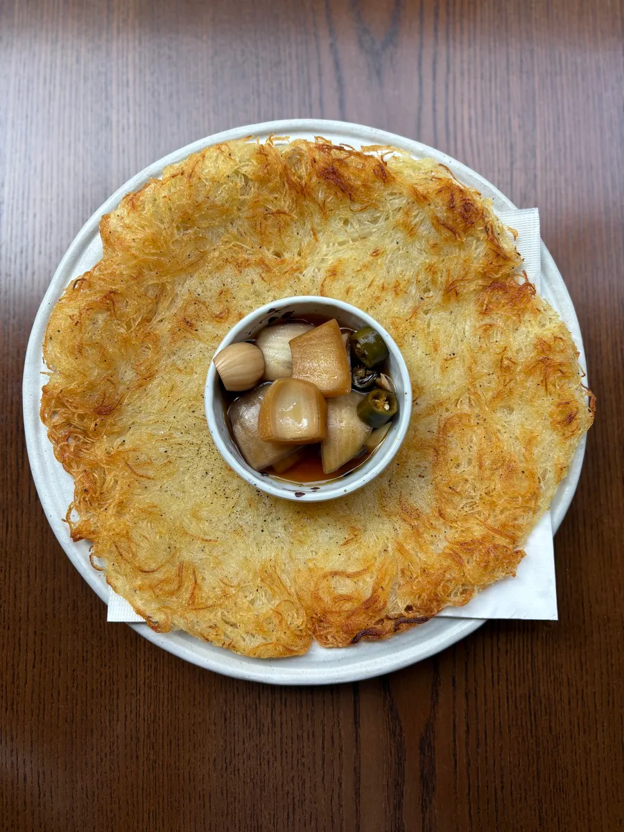 괸당 신당본점 감자채전. 접시를 꽉 채운 한 장이 담겼고 가장자리는 갈색으로 바삭하게 튀겨졌다. 가운데 종지에 간장과 마늘, 청양고추가 담겨 있다.