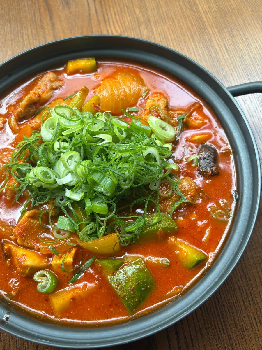 괸당 신당본점의 붉은 국물 찌개 한 냄비. 파채가 수북이 얹혔고 애호박과 양파, 청양고추가 보인다. 메뉴 이름은 사진에 적혀 있지 않다.