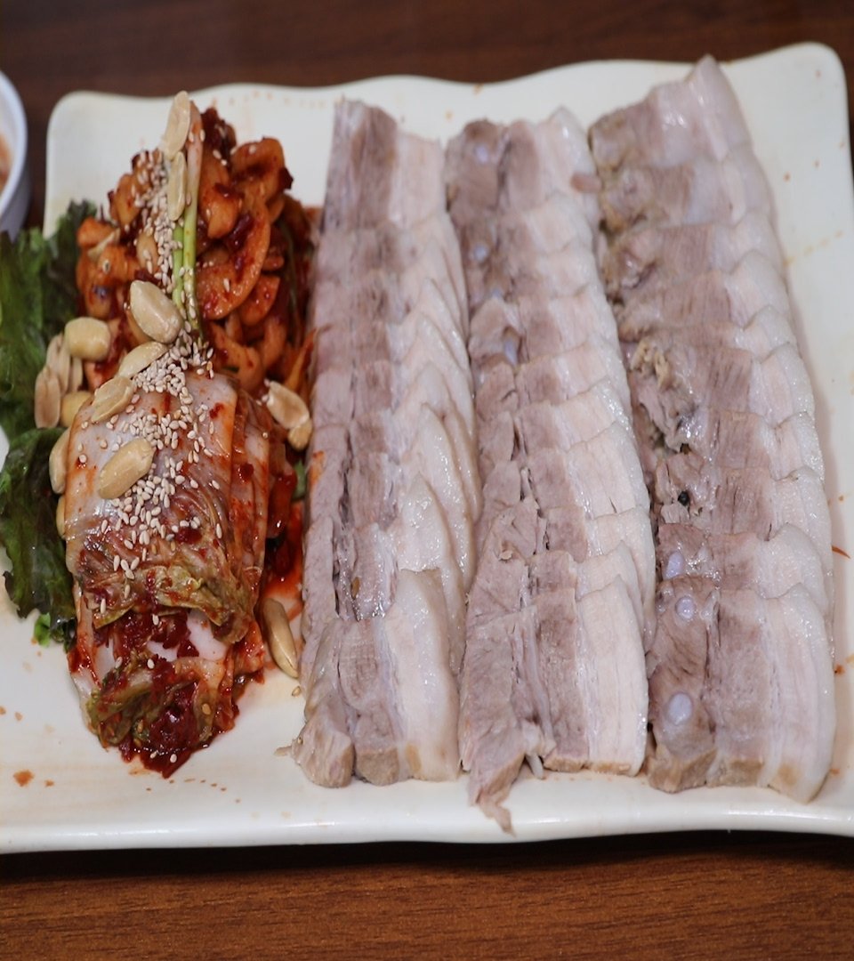 흰 접시에 수육이 세 줄로 눕고 옆에 땅콩 얹은 김치 말이가 놓였다
