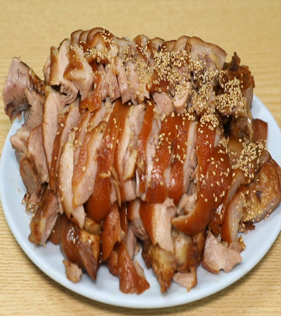 흰 접시에 껍질 붙은 족발 편육이 수북이 쌓였고 깨가 뿌려져 있다