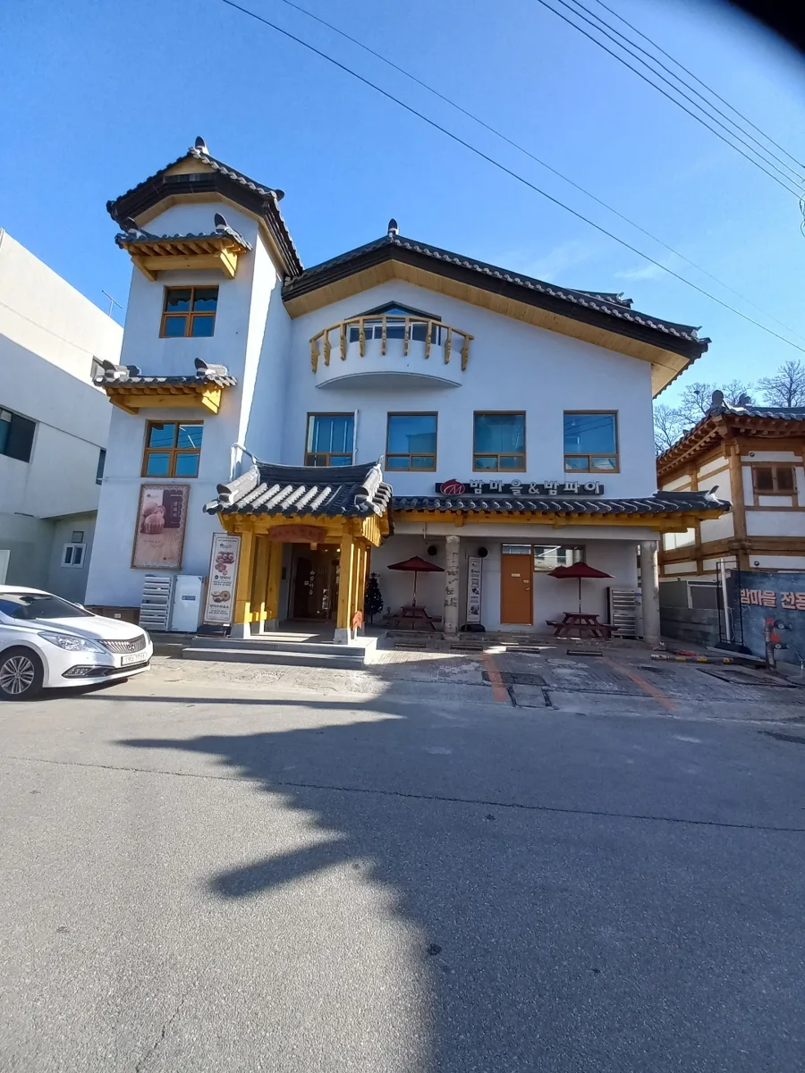 베이커리 밤마을 낮 외관. 간판 밤마을&밤파이, 앞에 파라솔 두 개와 나무 탁자